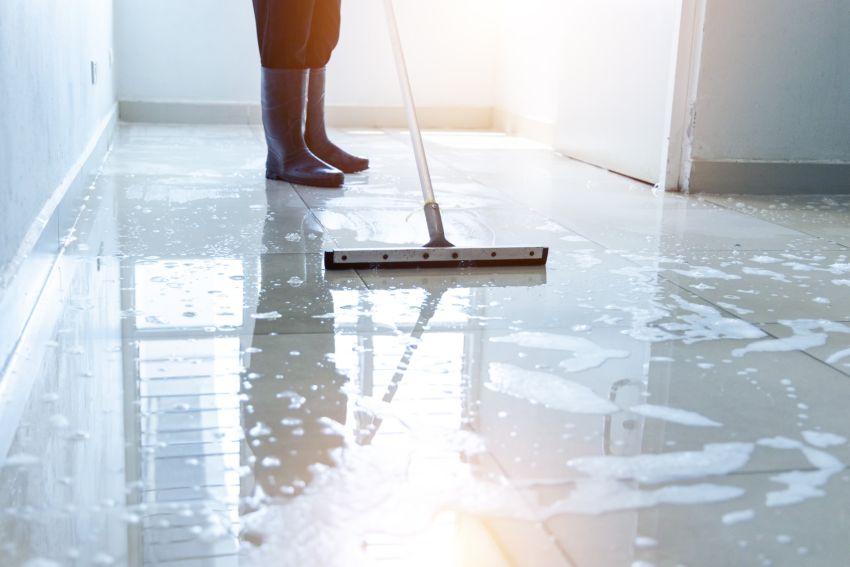 Cleaner mopping a wet office hallway floor with a squeegee mop